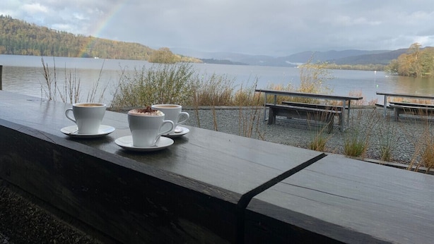A wooden bench with two white cups of coffee and a bench with a view of a lake and mountains. - Two minute walk from the World of Beatrix Potter, apartment with parking (Bowness-on-Windermere)