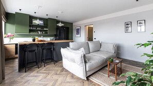 Una sala de estar moderna con un sofá, una mesa de centro y una zona de cocina con taburetes de bar.