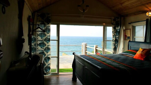 Een slaapkamer met een bed, uitzicht op de oceaan en een houten plafond.