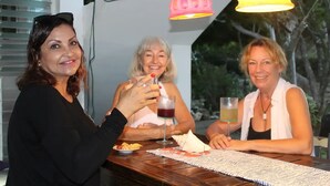Drie personen zitten aan een houten tafel met drankjes, onder hangende lampen.