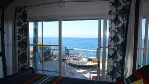 Een kamer met een grote schuifglazen deur die leidt naar een balkon met uitzicht op zee.