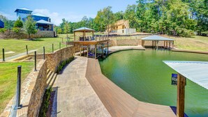 Ein Schwimmbad mit Holzterrassen und Gazebos, umgeben von Bäumen und einer Steinmauer.