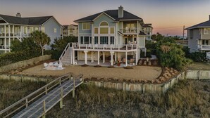 A beachfront property with a large house featuring a covered patio, multiple decks, and a wooden deck leading to the beach. - Paradise Found: Waterfront Escape with Dock, Firepit, and Sunsets Galore! (Wrightsville Beach)