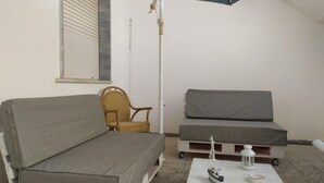 Ein Zimmer mit einer grauen Couch, einem Korbsessel, einem kleinen Tisch mit einem Schiffmodell und einem weißen Laternen.