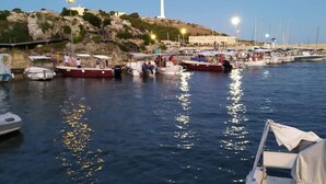 Ein Yachthafen mit vertäuten Booten, ein Leuchtturm im Hintergrund und ein felsiger Hügel.