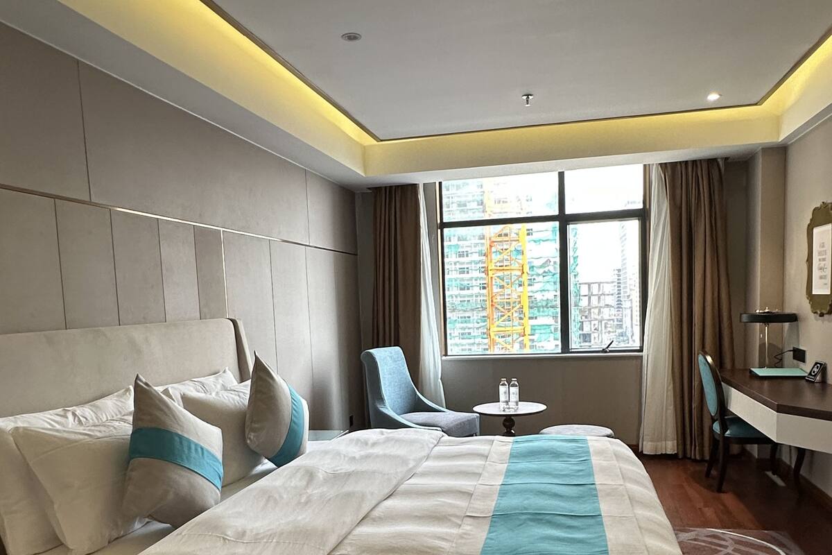 Una habitación de hotel moderna con una cama grande, un escritorio y vistas de la ciudad a través del ventanal.
