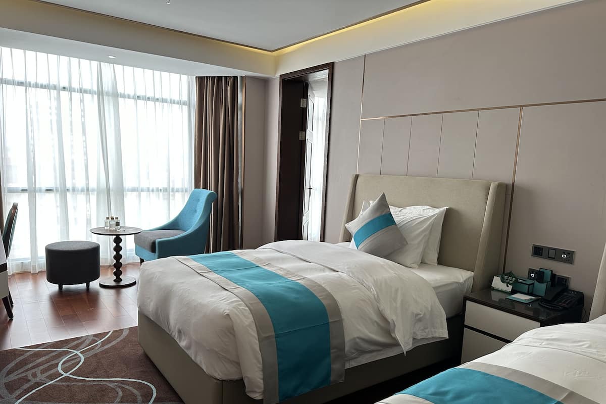 Un moderno cuarto de hotel con una cama grande, una mesita de noche, una silla y vistas al exterior a través de amplios ventanales.