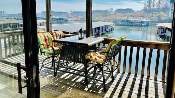 A covered outdoor seating area with a table and chairs, overlooking a body of water and docked boats. - Condo with Indoor Pool and Hot Tub! (Village of Four Seasons)