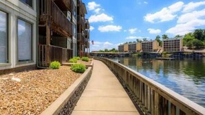 A waterfront walkway with buildings on one side and a canal on the other. - Condo with Indoor Pool and Hot Tub! (Village of Four Seasons)