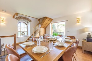 A dining area with a wooden table set for four, leather chairs, a staircase, and a view of greenery outside.