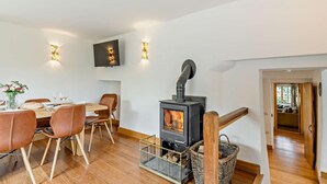 En matplats med ett bord för fyra personer, en vedeldad kamin och en tv som är monterad på väggen.
