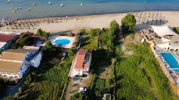 Vista aérea de una propiedad costera con piscina, sombrillas de playa y embarcaciones.