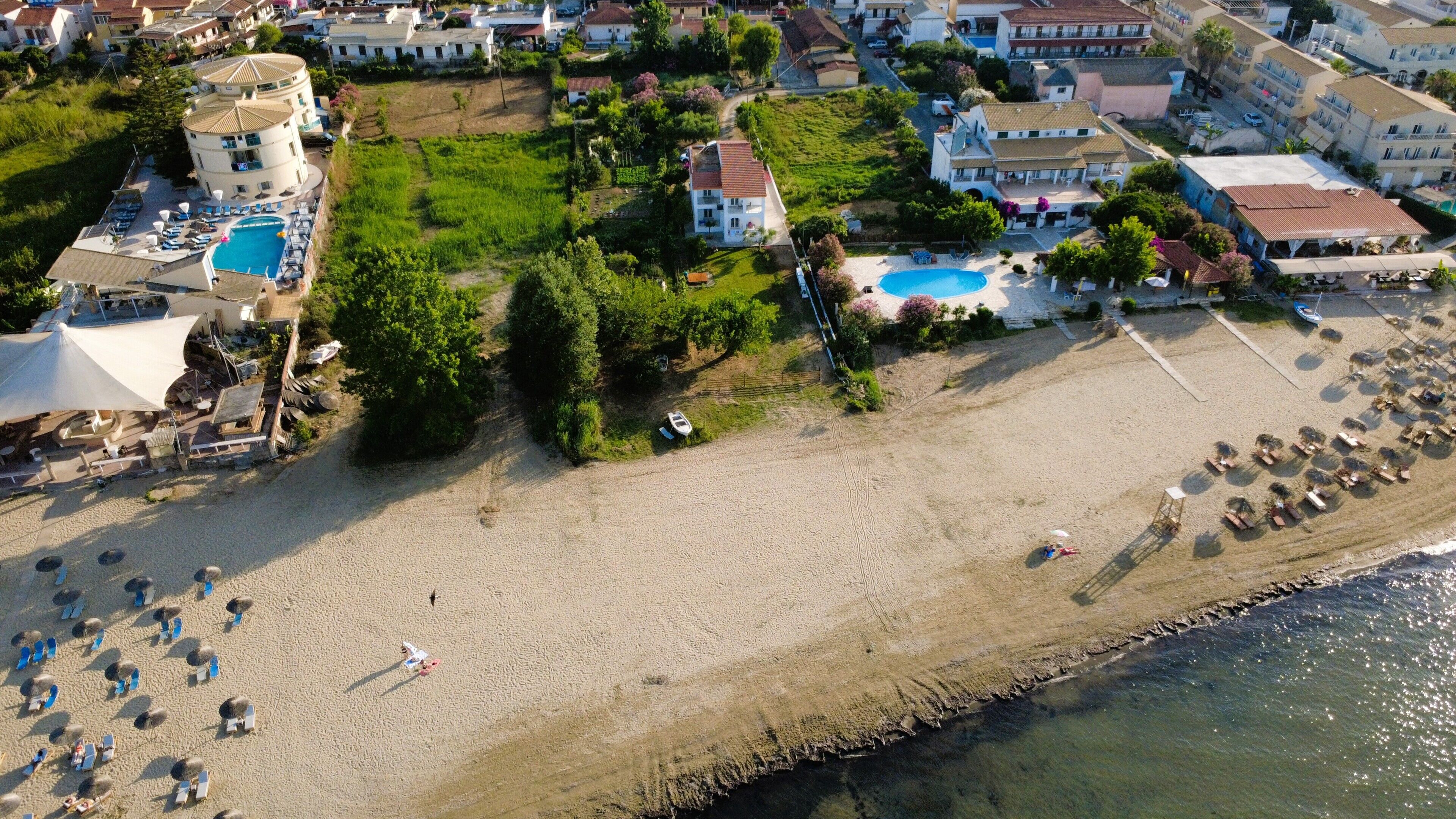 Vista aérea de una zona costera con playa arenosa, piscina y edificios residenciales.