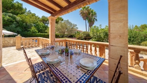 An outdoor dining area with a table set for four, surrounded by stone pillars and a wooden pergola. - Villa Victoria Alcudia Alcudia Bonaire for 6 with pool (Alcúdia)