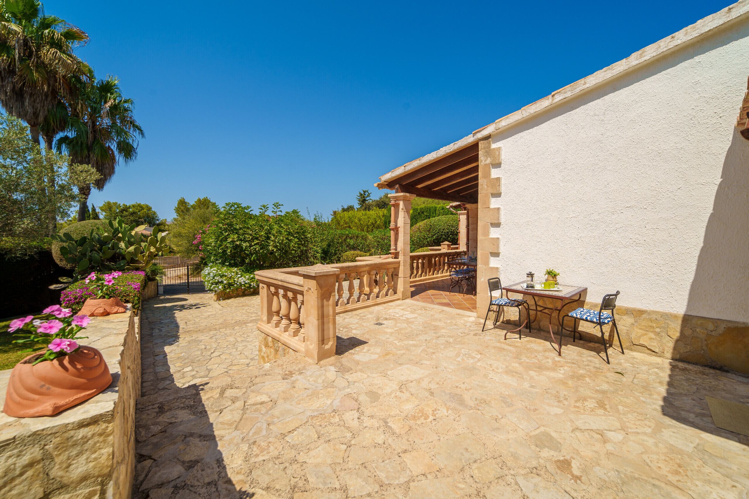 Un patio in pietra con tavolo e sedie, circondato da piante in vaso e un muro bianco.