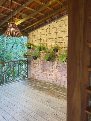 Enjoy the serene atmosphere on this balcony with a brick wall, wooden floor, and lush greenery.