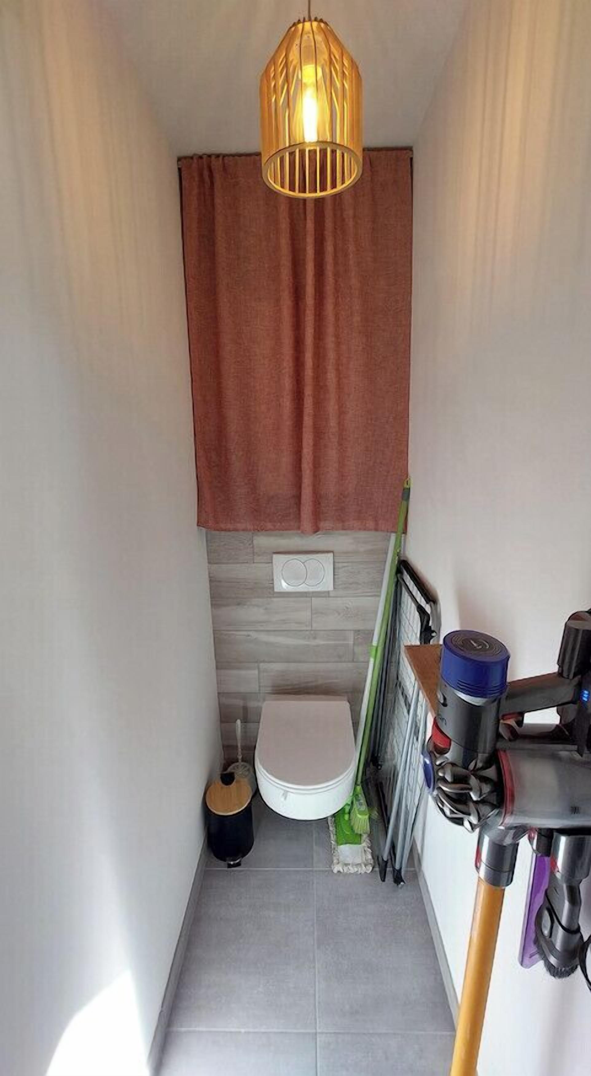 A small bathroom with a toilet, a shower area, a towel, and cleaning supplies.