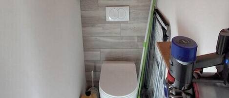A small bathroom with a toilet, a shower area, a towel, and cleaning supplies.