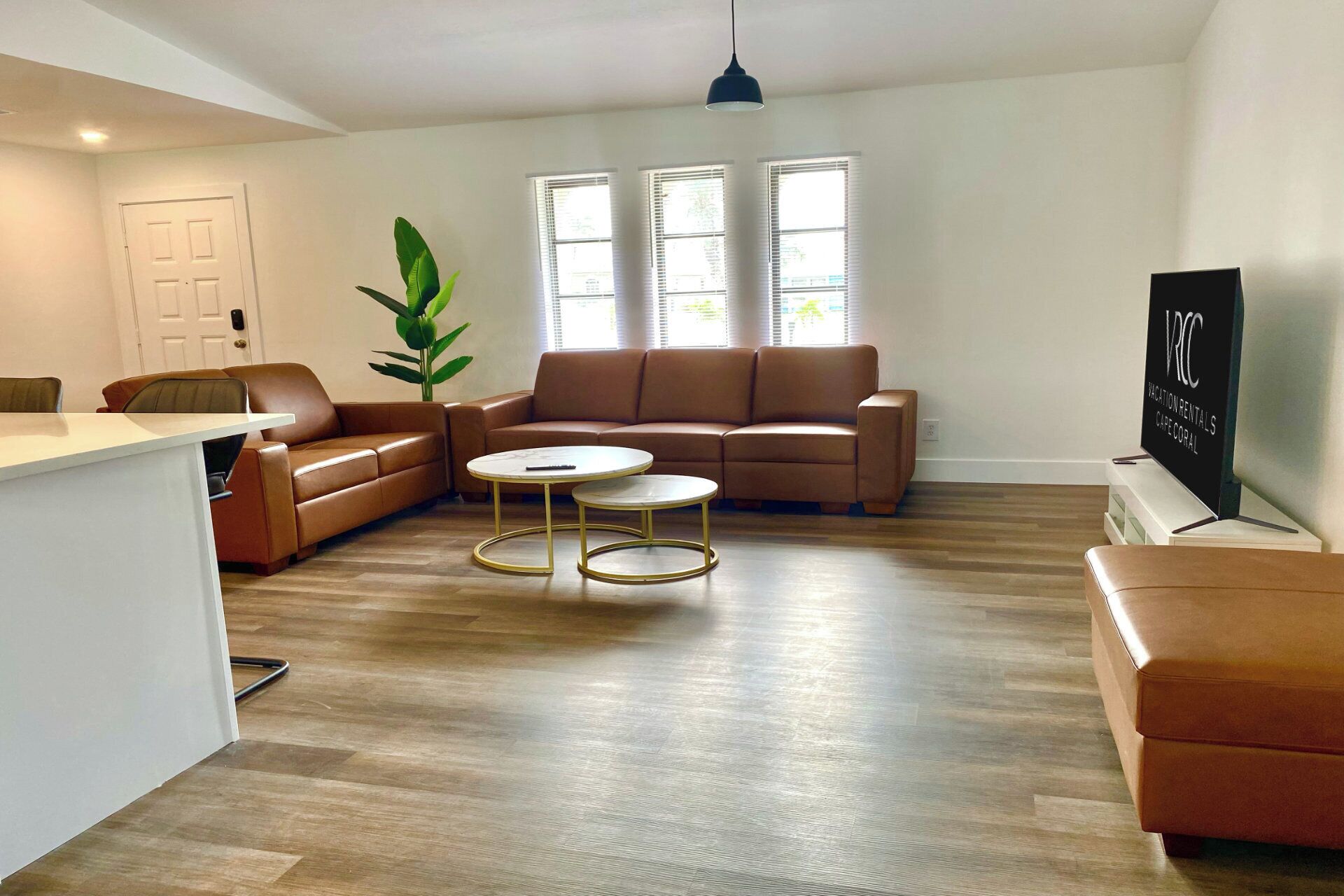 A modern living room with a brown leather sofa, a white coffee table, and a TV on a stand.