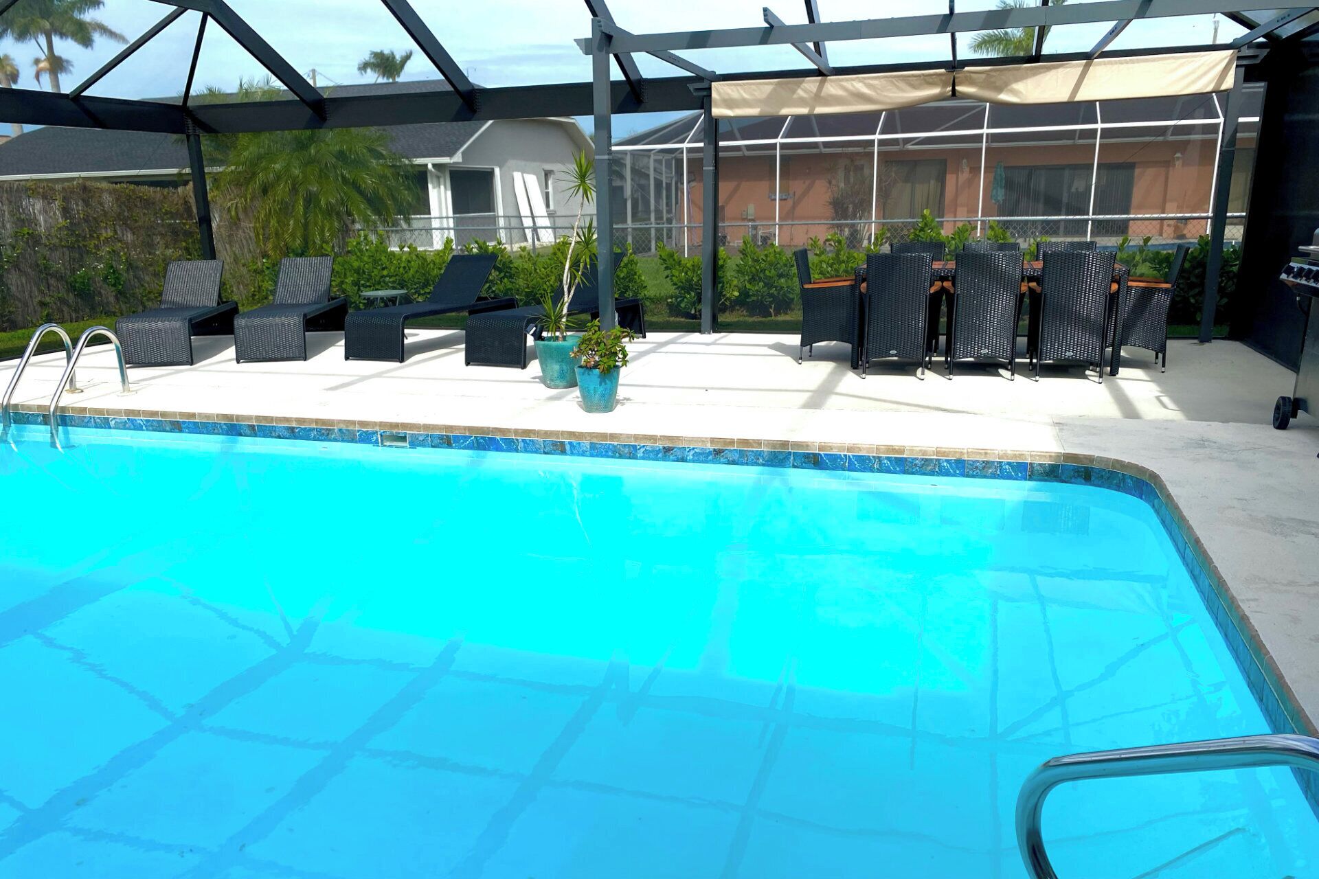 A swimming pool with lounge chairs and potted plants, surrounded by a covered patio area.