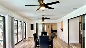 A modern interior with a dining area, a ceiling fan, and a pool visible through the glass doors. - VRCC Villa The Rocks - where luxury meets beauty (Cape Coral)