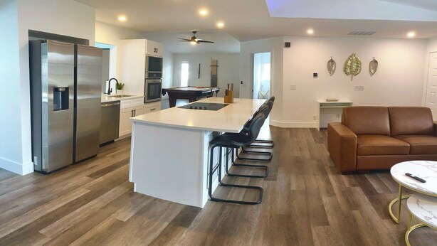 A modern kitchen with a central island, stainless steel appliances, and a dining area with a brown leather couch and a small round table. - VRCC Villa The Rocks - where luxury meets beauty (Cape Coral)