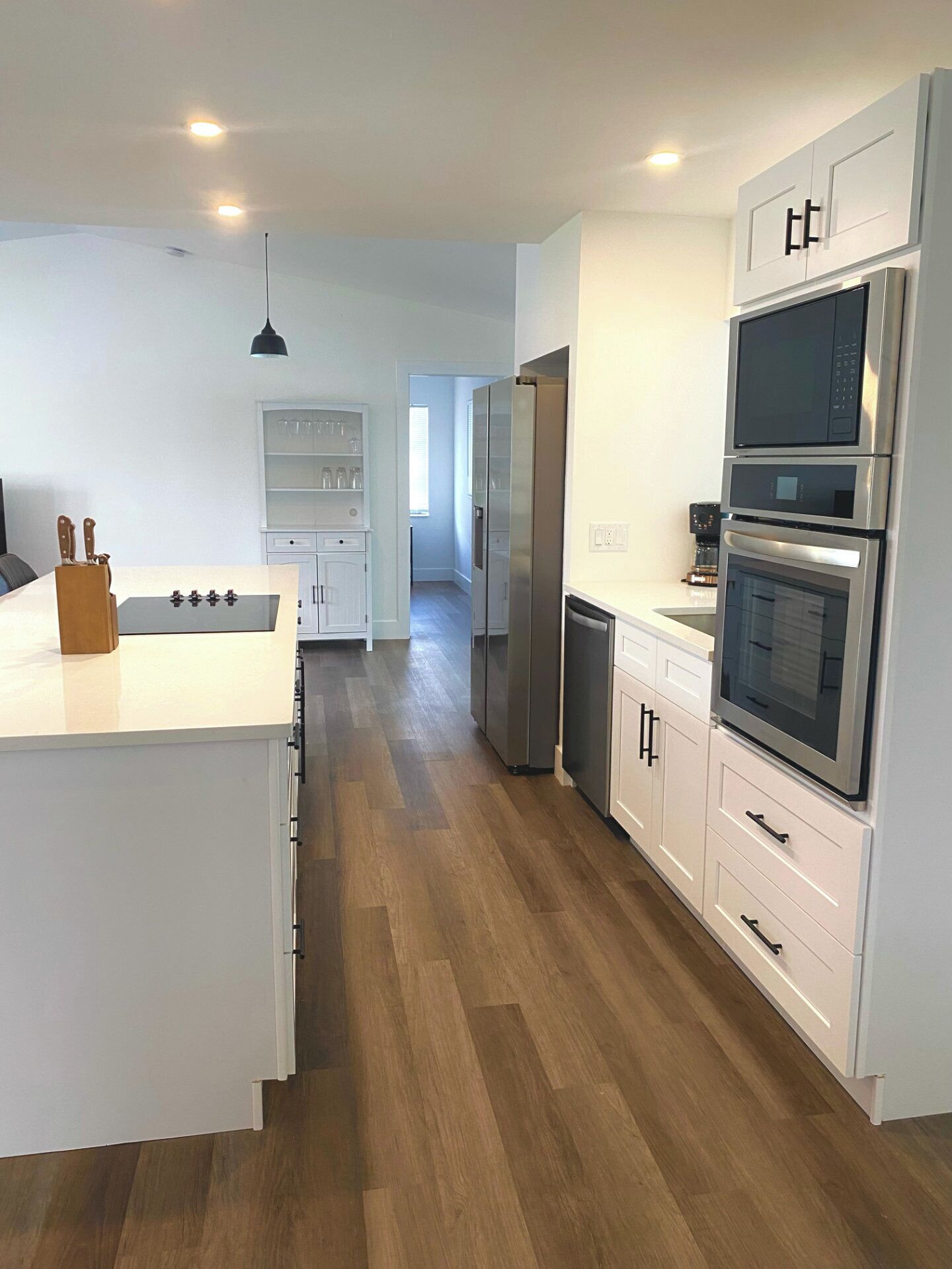 Eine moderne Küche mit weißen Schränken, einer zentralen Kochinsel und integrierten Geräten, darunter ein Kühlschrank, ein Backofen und eine Mikrowelle.
