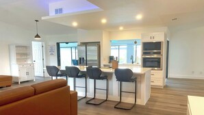 A modern kitchen with a central island, bar stools, and built-in appliances. - VRCC Villa The Rocks - where luxury meets beauty (Cape Coral)