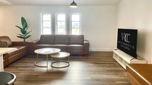 A modern living room with a brown leather sofa, two white round tables, and a large window with blinds. - VRCC Villa The Rocks - where luxury meets beauty (Cape Coral)