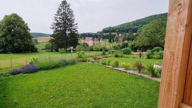 Een weelderig groen landschap met een grote boom, een verzorgd gazon en een gebouw met een toren in de verte.