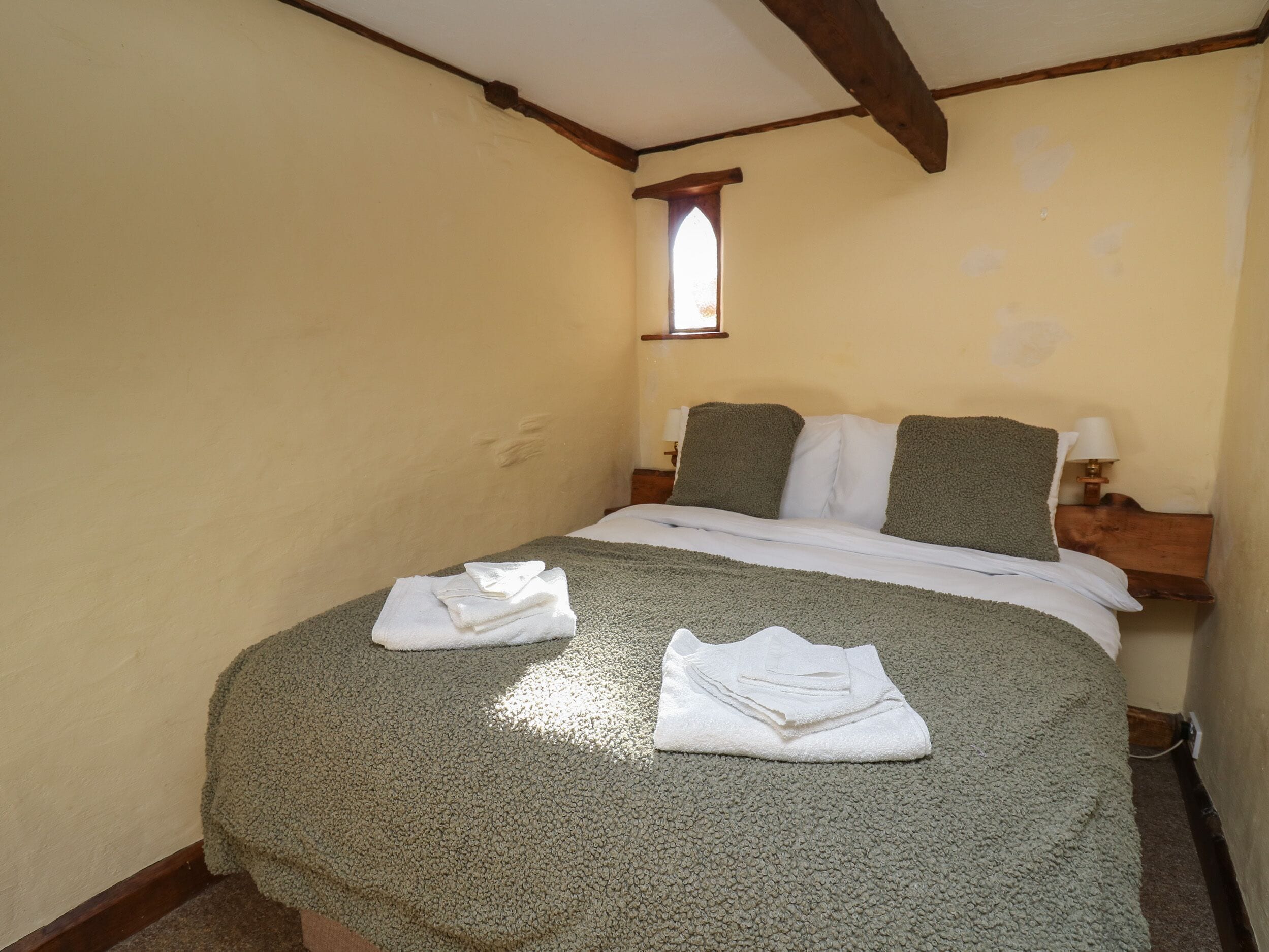 A room with a bed, two pillows, a window, and a lamp.