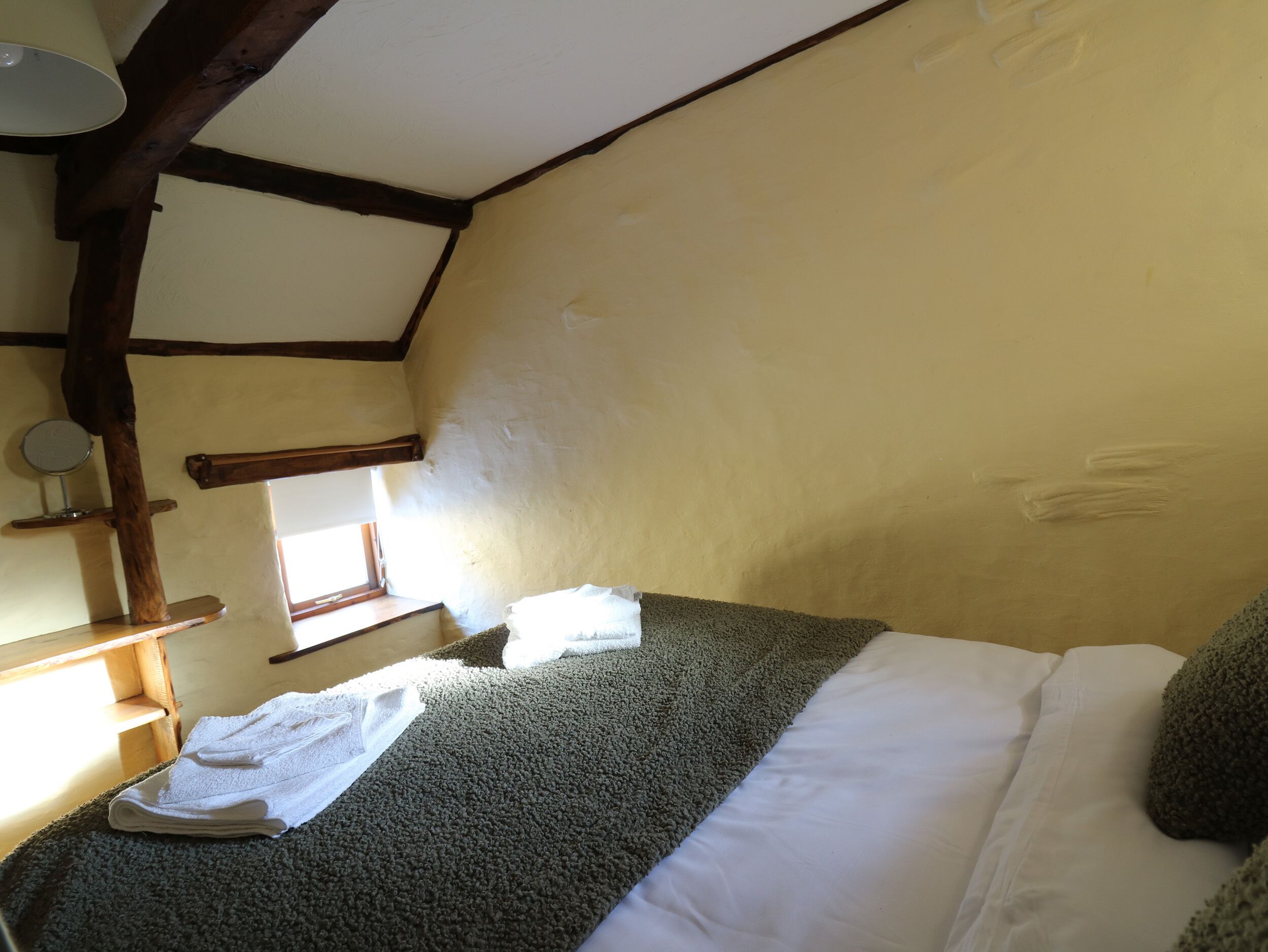 A room with a bed, a window, a wooden beam ceiling, and a towel on the floor.