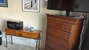 A bedroom with a bed, a dresser, a microwave, a television, and a vacuum cleaner.