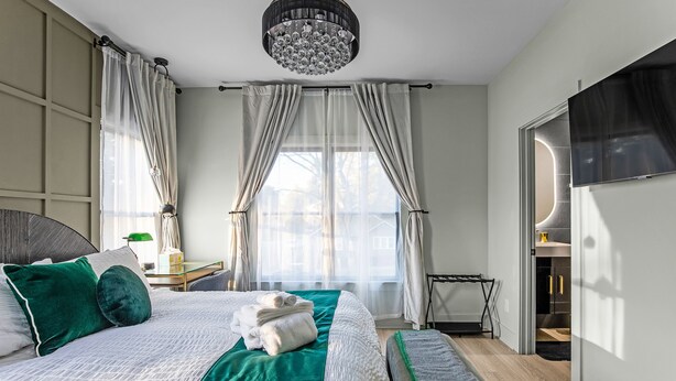 Ett modernt hotellrum med en stor säng, en kristallkrona och utsikt över omgivningarna.