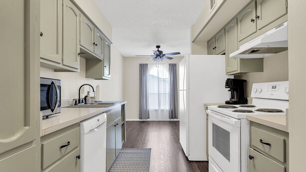 A narrow kitchen with white appliances, a ceiling fan, and a window with curtains. - Entire Furnished rental unit in San Antonio, Texas

 (San Antonio)