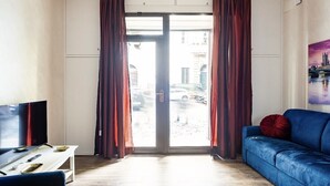 A room with a TV, a sofa, a coffee table, and a view of the street through a glass door. - 2 bedroom apartment in rome (Roma)