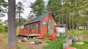 A cabin with a stone chimney, wooden deck, and red Adirondack chairs. - Rustic Log Cabin Near Jack Frost and Lake Harmony (Blakeslee)