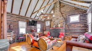 A log cabin interior with wooden floors, a stone wall, a wooden ceiling, a wooden rocking chair, a sofa, a table, and a television. - Rustic Log Cabin Near Jack Frost and Lake Harmony (Blakeslee)