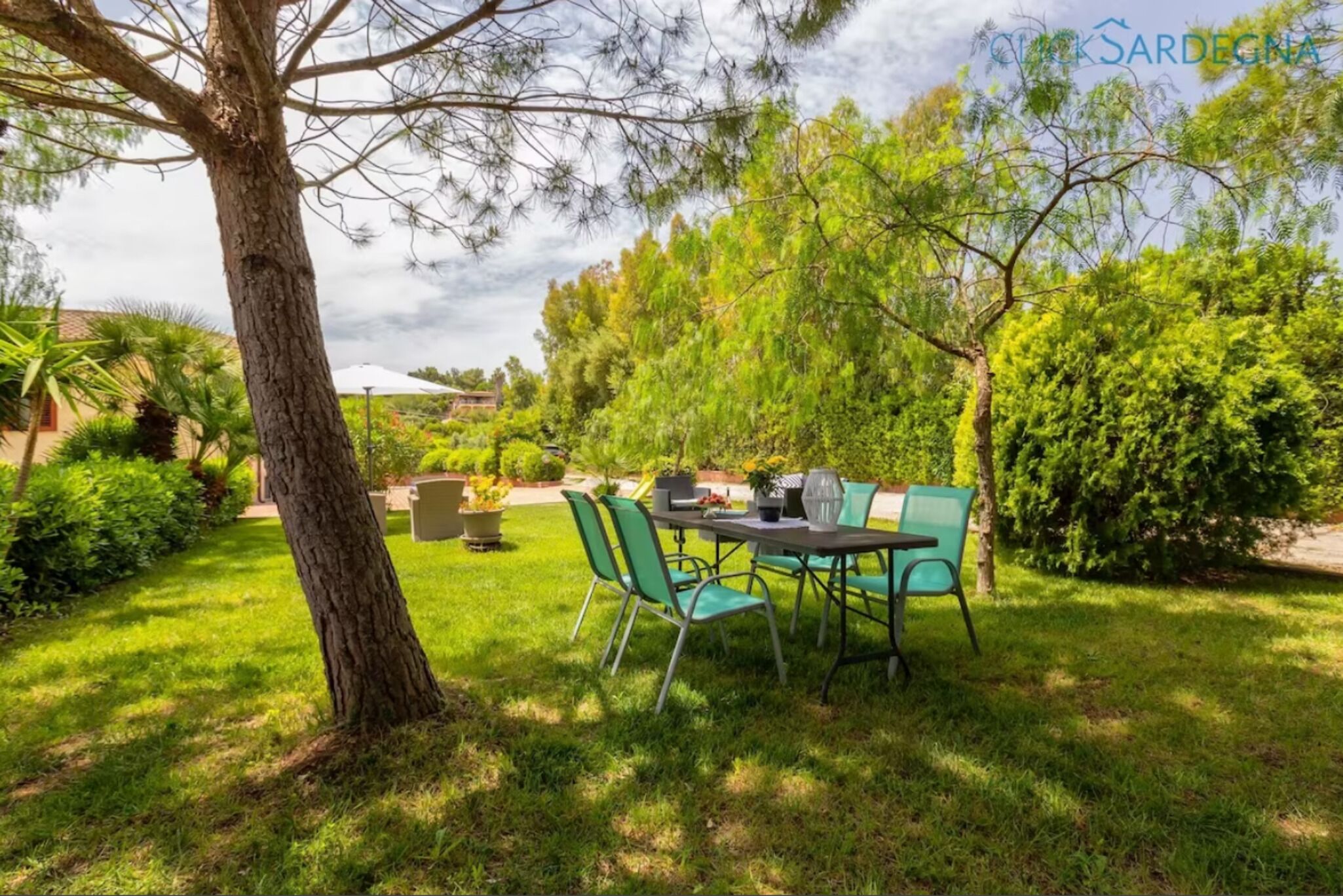 An outdoor seating area with a table and chairs, surrounded by greenery and trees.