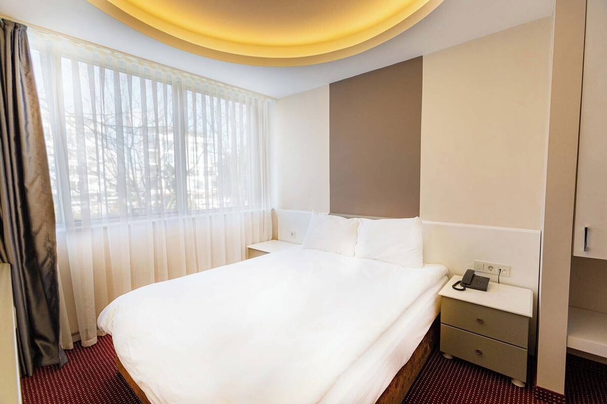 A hotel room with a large bed, a bedside table with a phone, and a wardrobe.