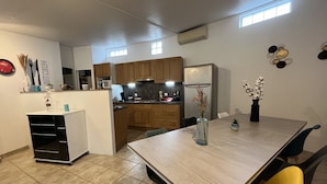 A modern kitchen with wooden cabinets, a built-in microwave, and a refrigerator. There is a dining table with chairs and a vase with flowers.
