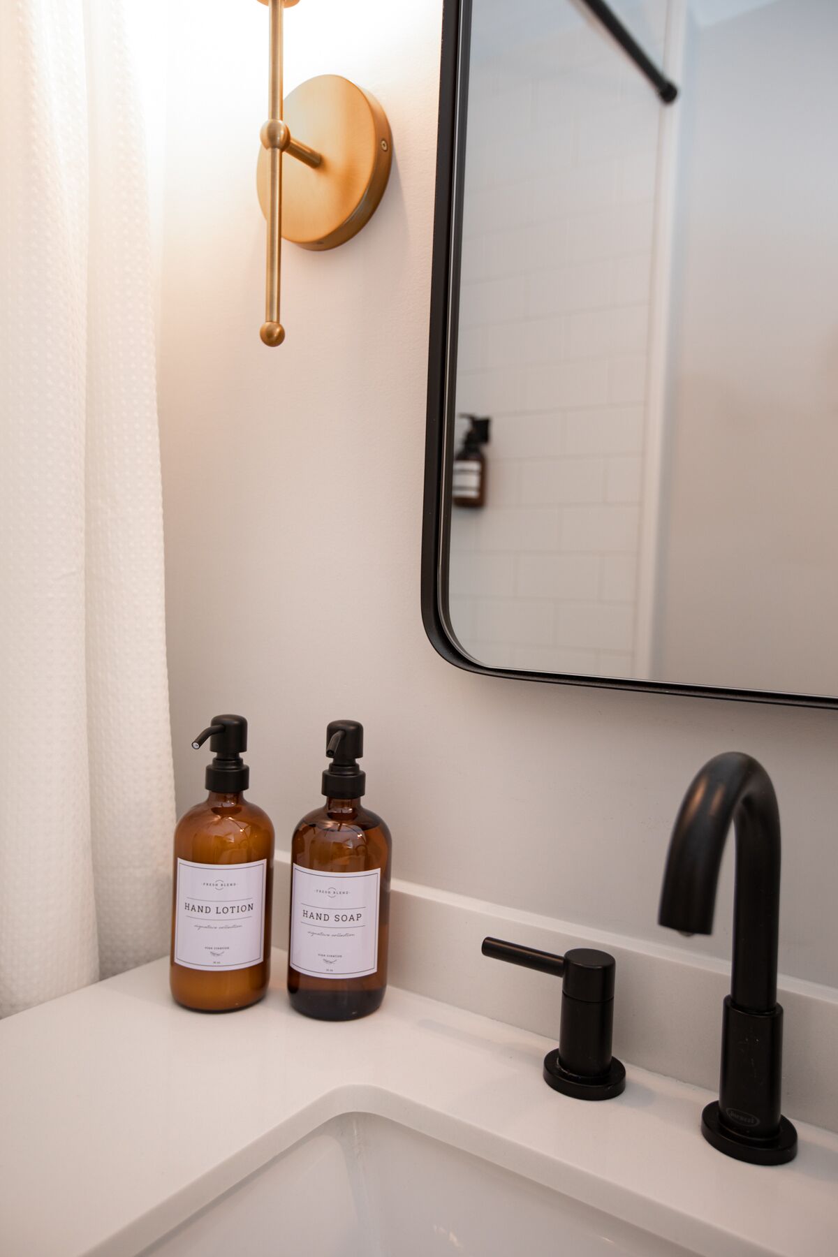 A bathroom sink with two bottles of hand lotion and soap, a black faucet, and a mirror with a gold handle.