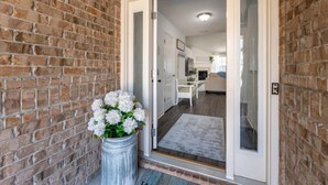 A brick exterior wall with a white door leading to a modern kitchen and living area. - Heated Pool | Minutes to Navarre Beach | 2 Kings (Navarre)