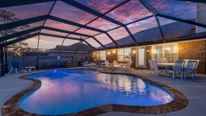 An outdoor swimming pool with a stone border, surrounded by lounge chairs and a covered patio area with a view of the sunset. - Heated Pool | Minutes to Navarre Beach | 2 Kings (Navarre)