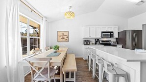 A modern kitchen with white cabinetry, a stainless steel refrigerator, and a dining area with a wooden table and chairs. - Heated Pool | Minutes to Navarre Beach | 2 Kings (Navarre)