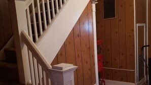 Un interior de madera con una escalera blanca, escalones alfombrados y un objeto rojo en el suelo.