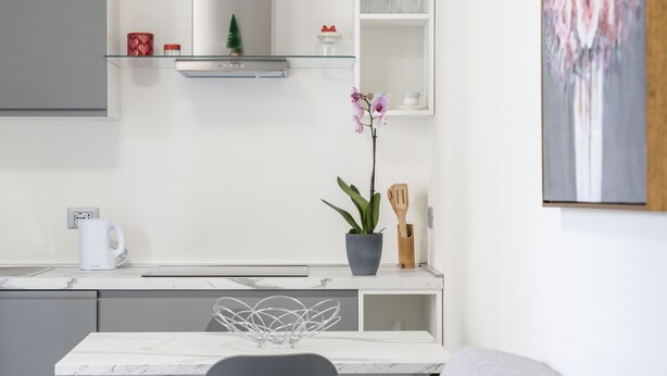 Cuina moderna amb taulell de marbre, taula de dinar blanca i una orquídia en test.