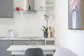 Uma cozinha moderna com bancada de mármore, mesa de jantar branca e uma orquídea em vaso.