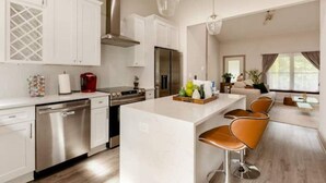 A modern kitchen with white cabinetry, stainless steel appliances, and a central island with bar stools. - Luxe Bungalow in Downtown Decatur / 2BD 2 BA (Decatur)