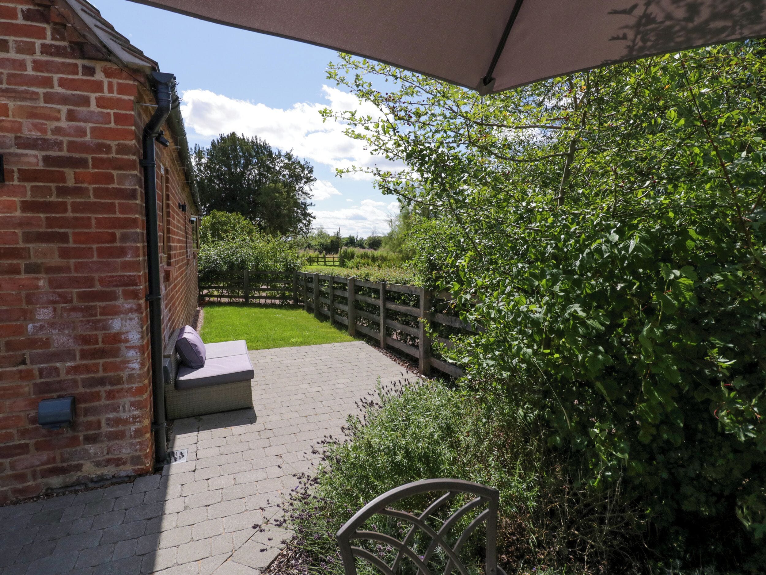 A covered outdoor area with a brick wall, a bench, and a pathway leading to a wooden fence.